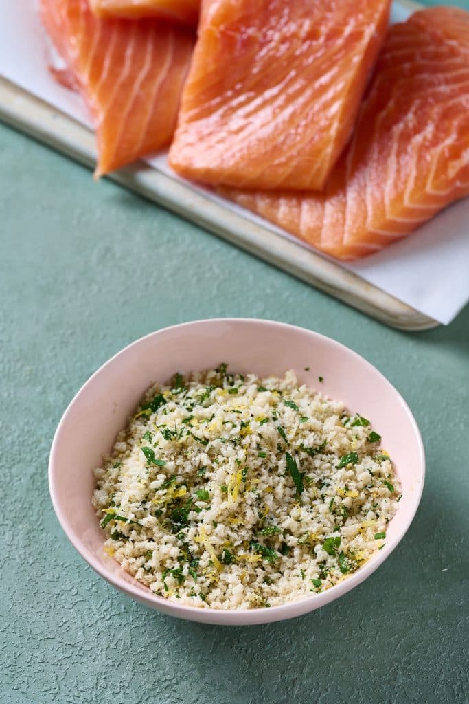 a bowl with a panko and herb mixture and fresh salmon fillets