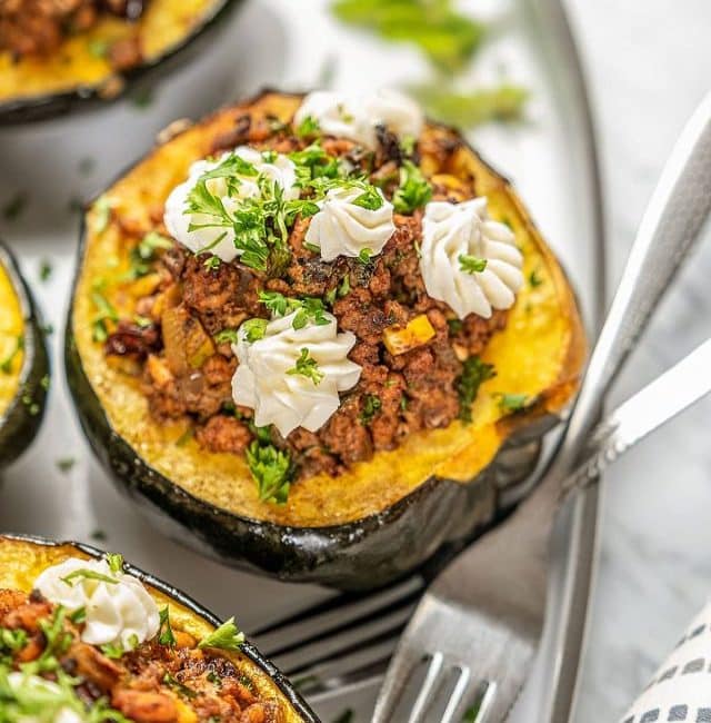 Stuffed acorn squashes topped with whipped cheese on a plate.
