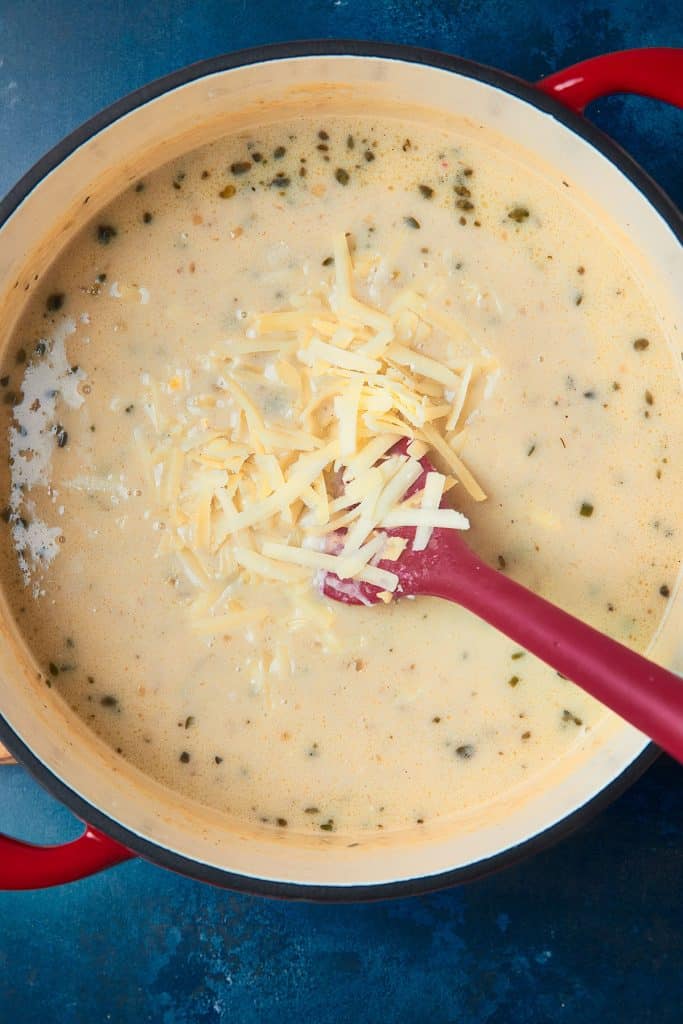 Adding shredded cheese into a pot of beer cheese soup 
