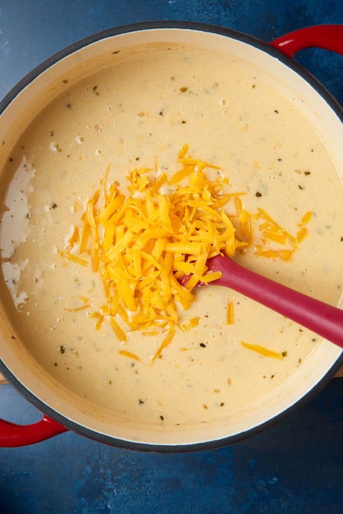 Adding shredded sharp cheddar cheese into a Dutch oven filled with beer and cheese soup