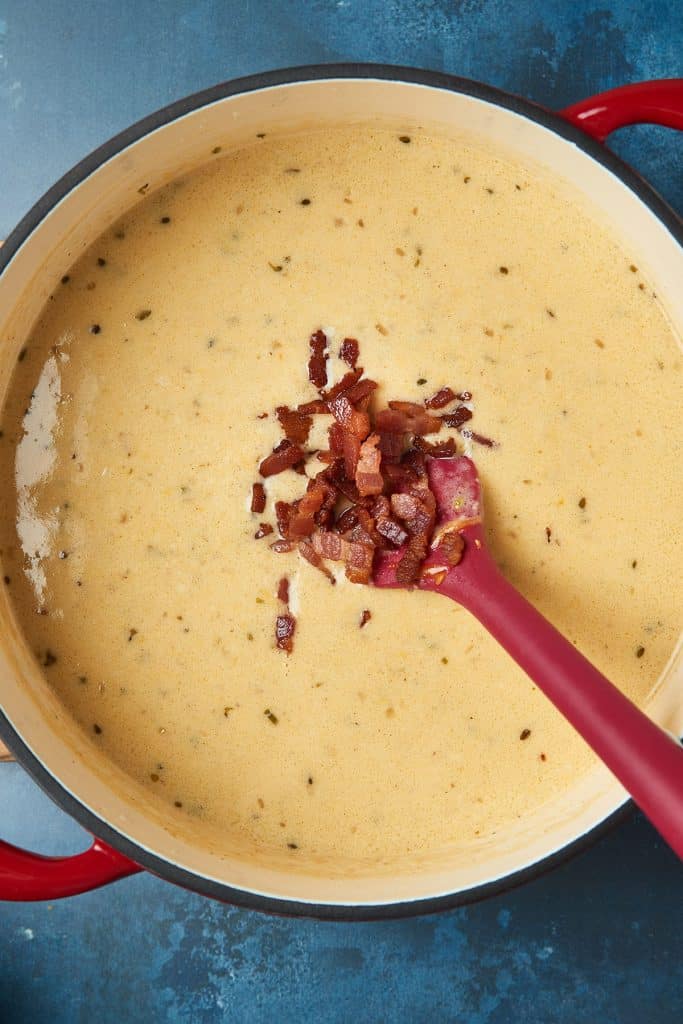 Adding crispy bacon into a pot of beer and cheese soup.