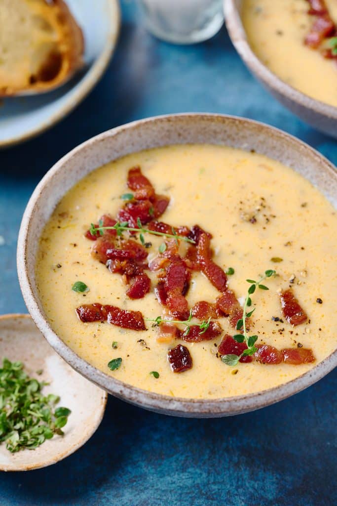 Bowl of creamy soup topped with crispy bacon and garnished with fresh thyme leaves