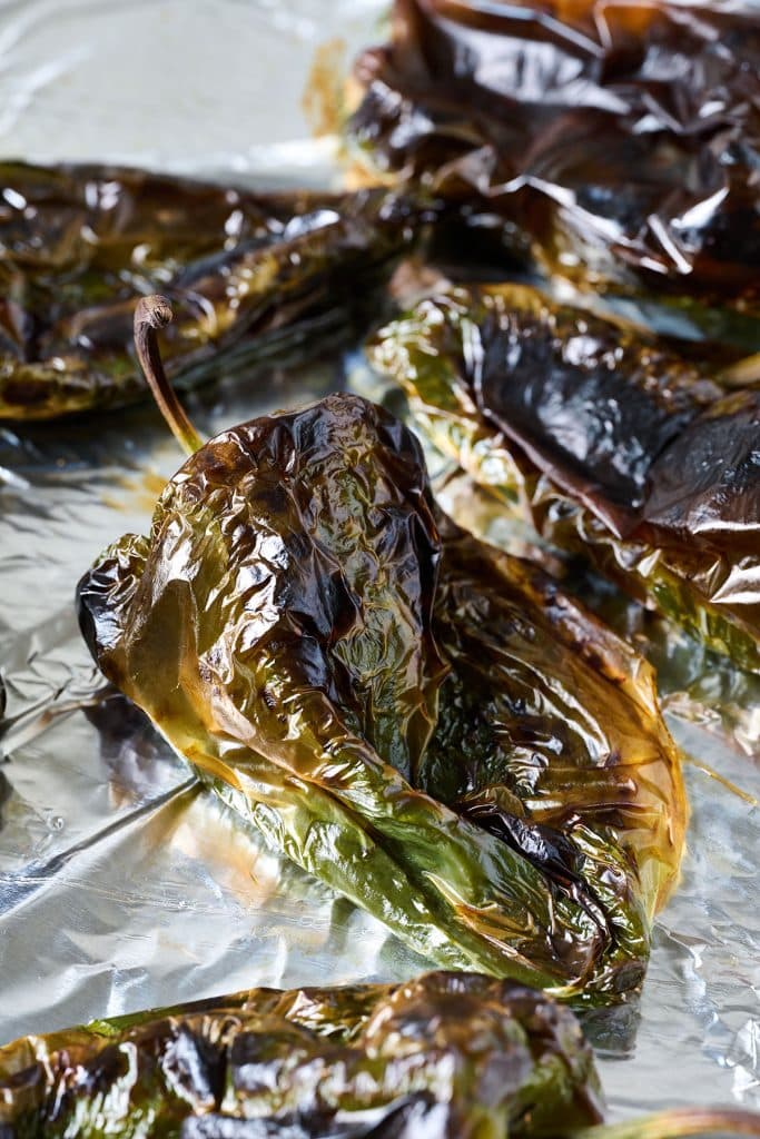 Nicely charred roasted poblano peppers on a baking sheet lined with aluminum foil.