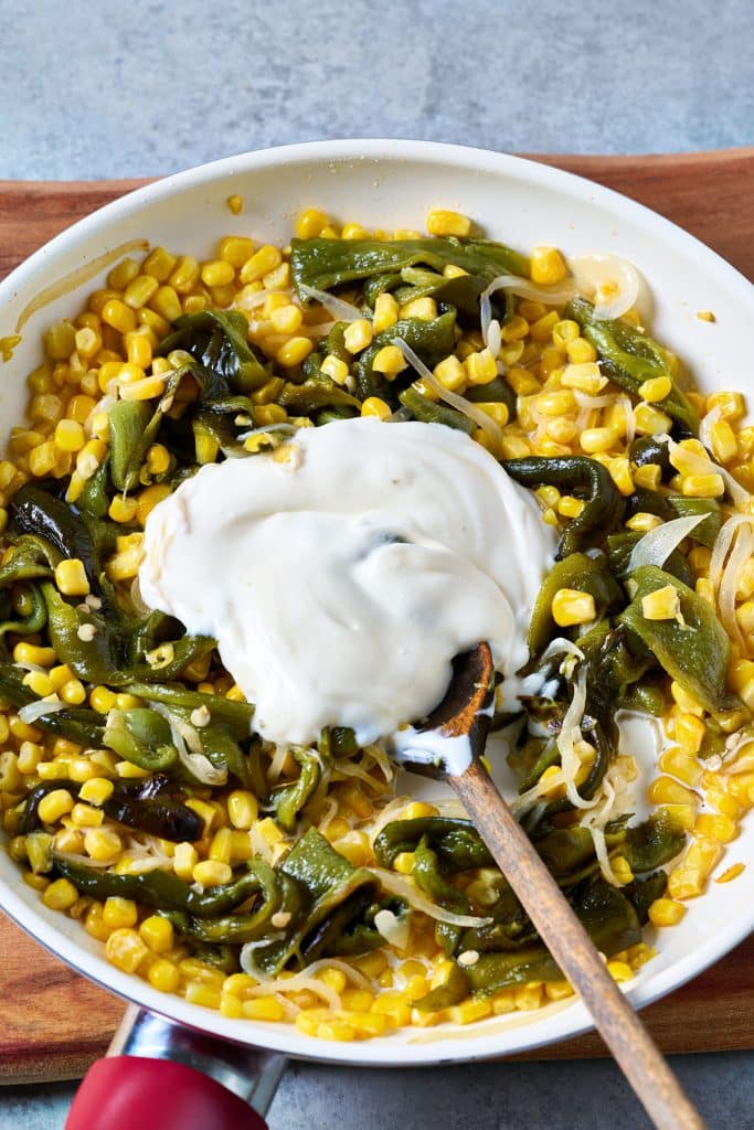 Mexican crema is added to a skillet to be combined with roasted poblano peppers, corn and onion.