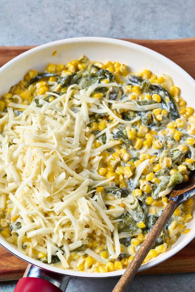 Creamy rajas topped with shredded cheese in a skillet