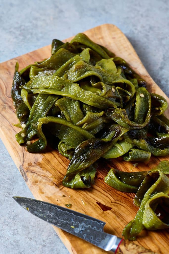 Peeled and roasted poblano peppers cut up into rajas (thin, long strips) on a cutting board.