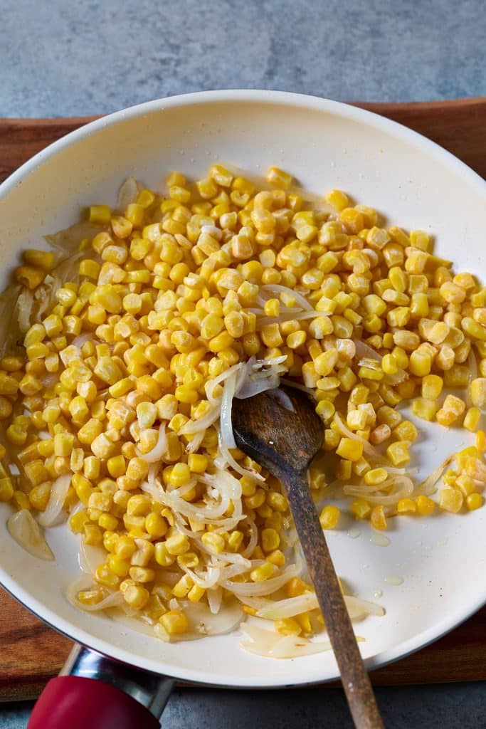 Corn added to a skillet with sautéed onions