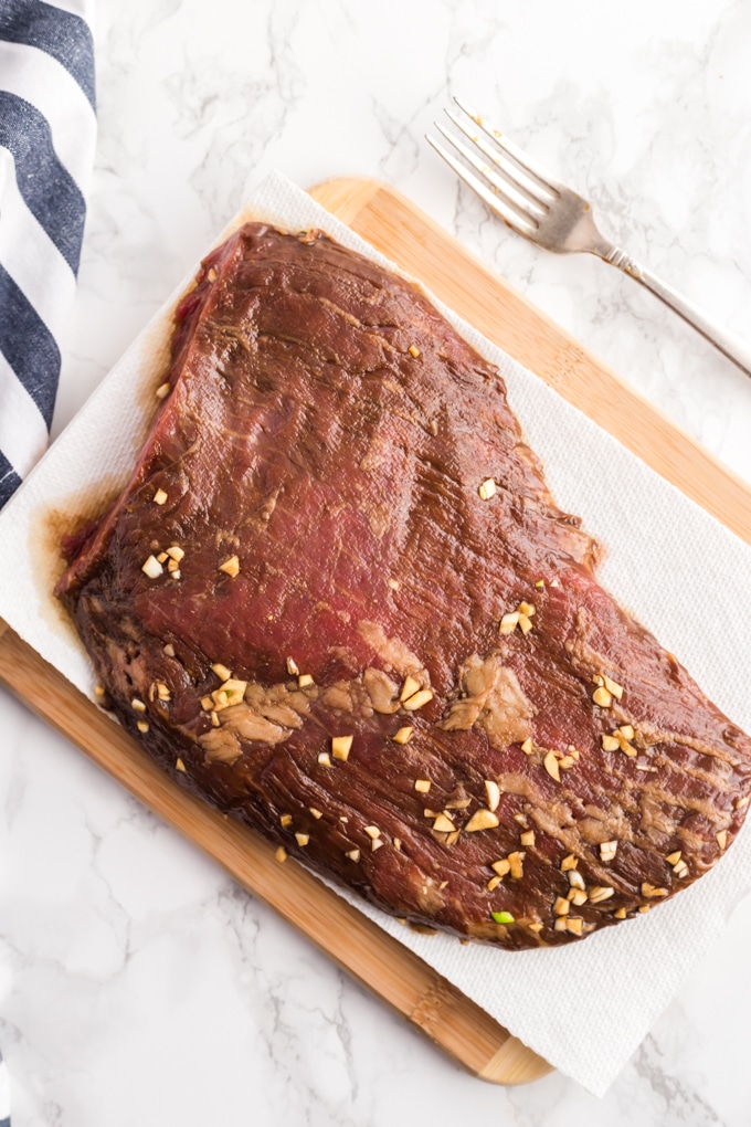 Marinated flank steak sitting on a board covered with paper towel.