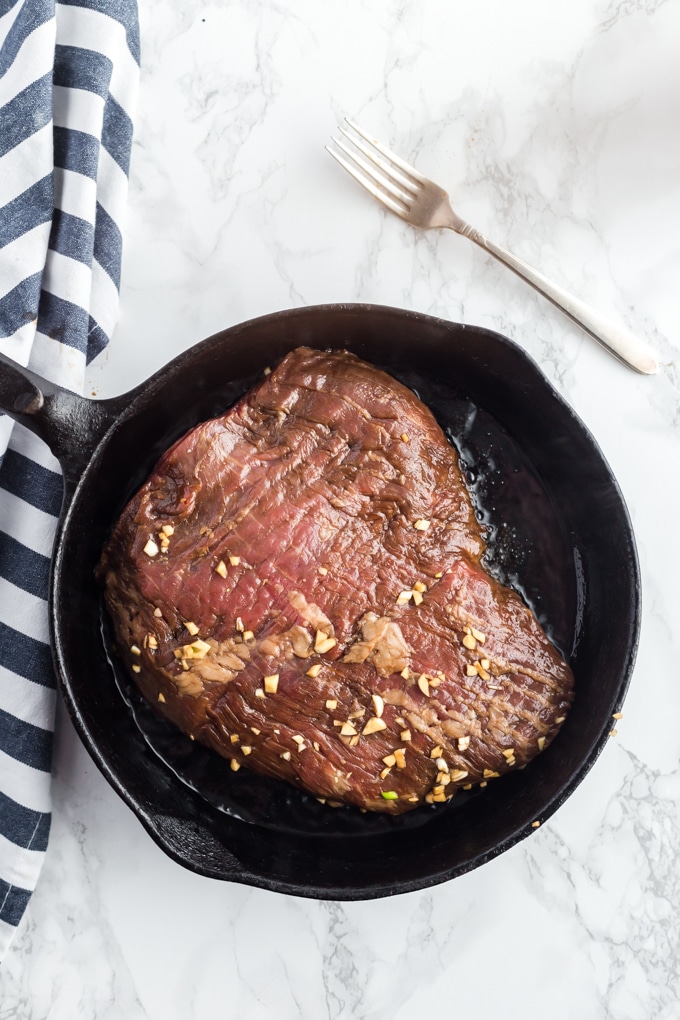 London broil cooking in a cast iron skillet.