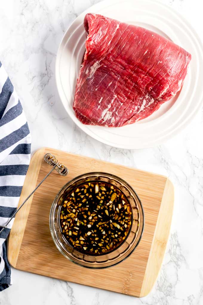 Raw flank steak roast next to a bowl with steak marinade