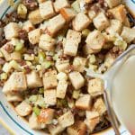 pouring chicken broth over the sautéed vegetables in the bowl with the sausage and the bread cubes.