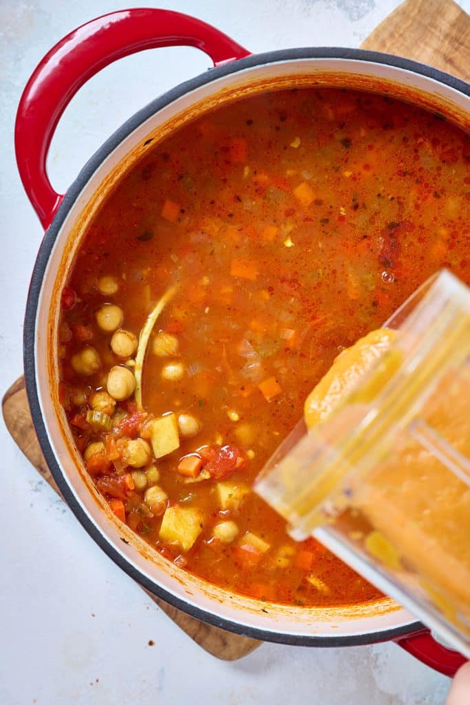 A portion of blended soup is added to a pot of chickpea and vegetable soup 