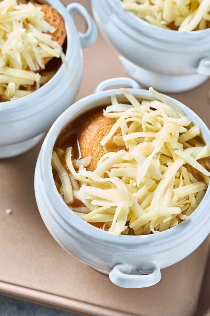 shredded cheese tops toasted bread set on top of a bowl of soup.