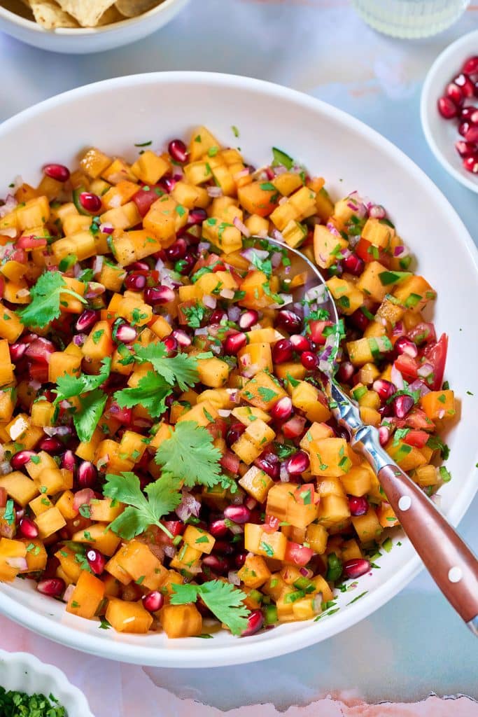 A bowl filled with persimmon salsa fresca garnished with pomegranate arils and fresh cilantro.