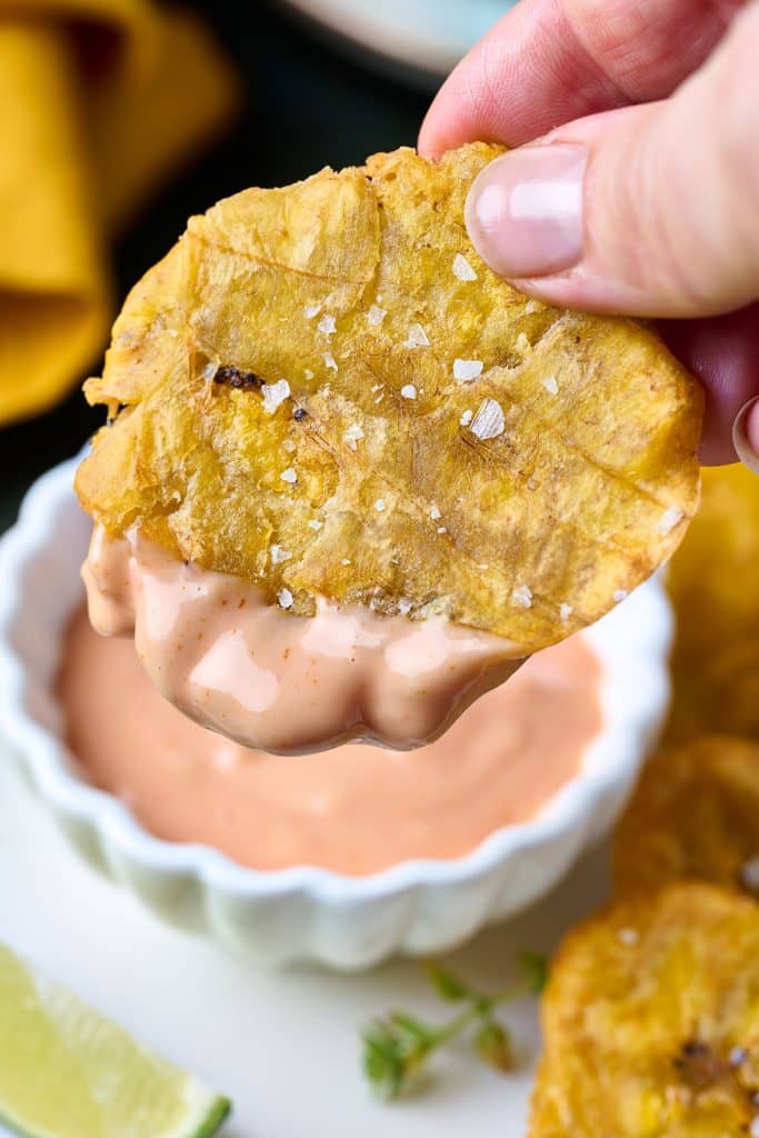Close up photo of fried plantain chip (tostone) with salt dipped in mayo ketchup (ketchup mayo)