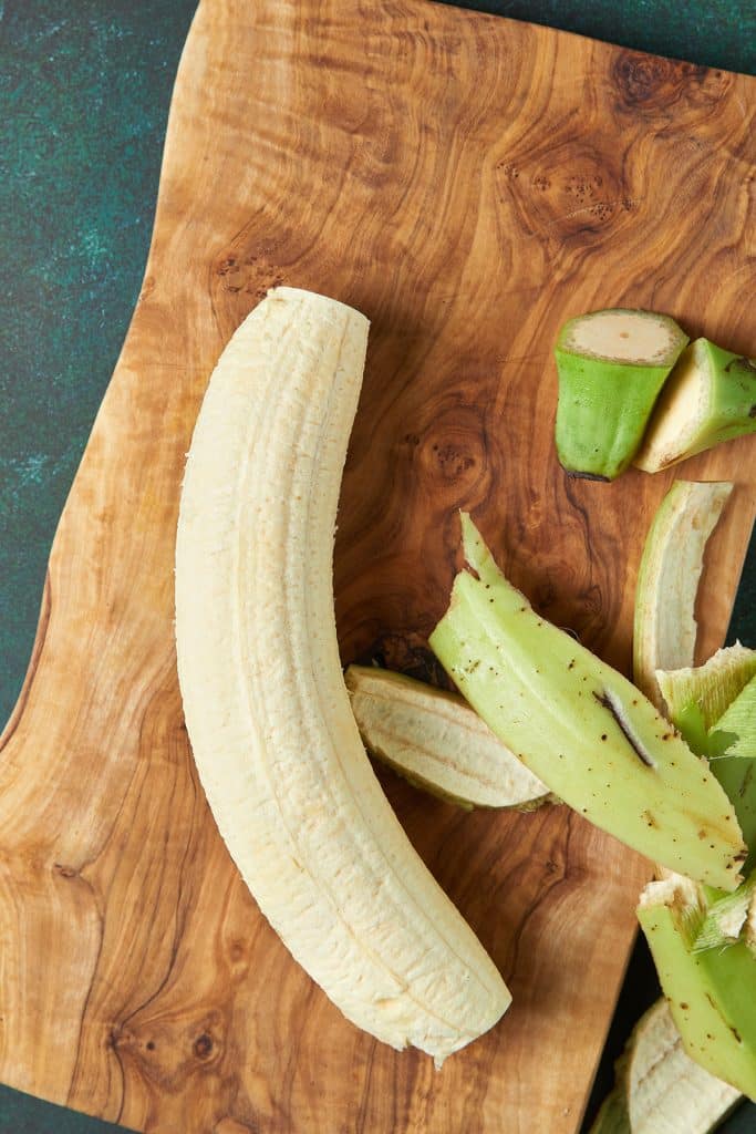 Skin and end removed from plantain laid on a cutting board