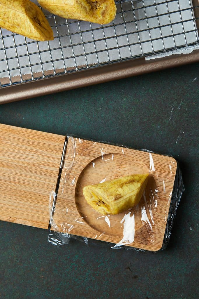 A yellow cooked plantain, placed onto a tostonera lined with plastic wrap.