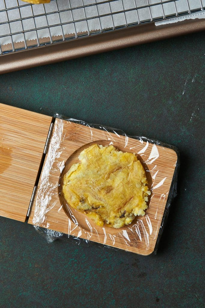 A smashed plantain coin on a tostonera with lined plastic wrap. The bottom of a glass or bottom of a plate can also be used.