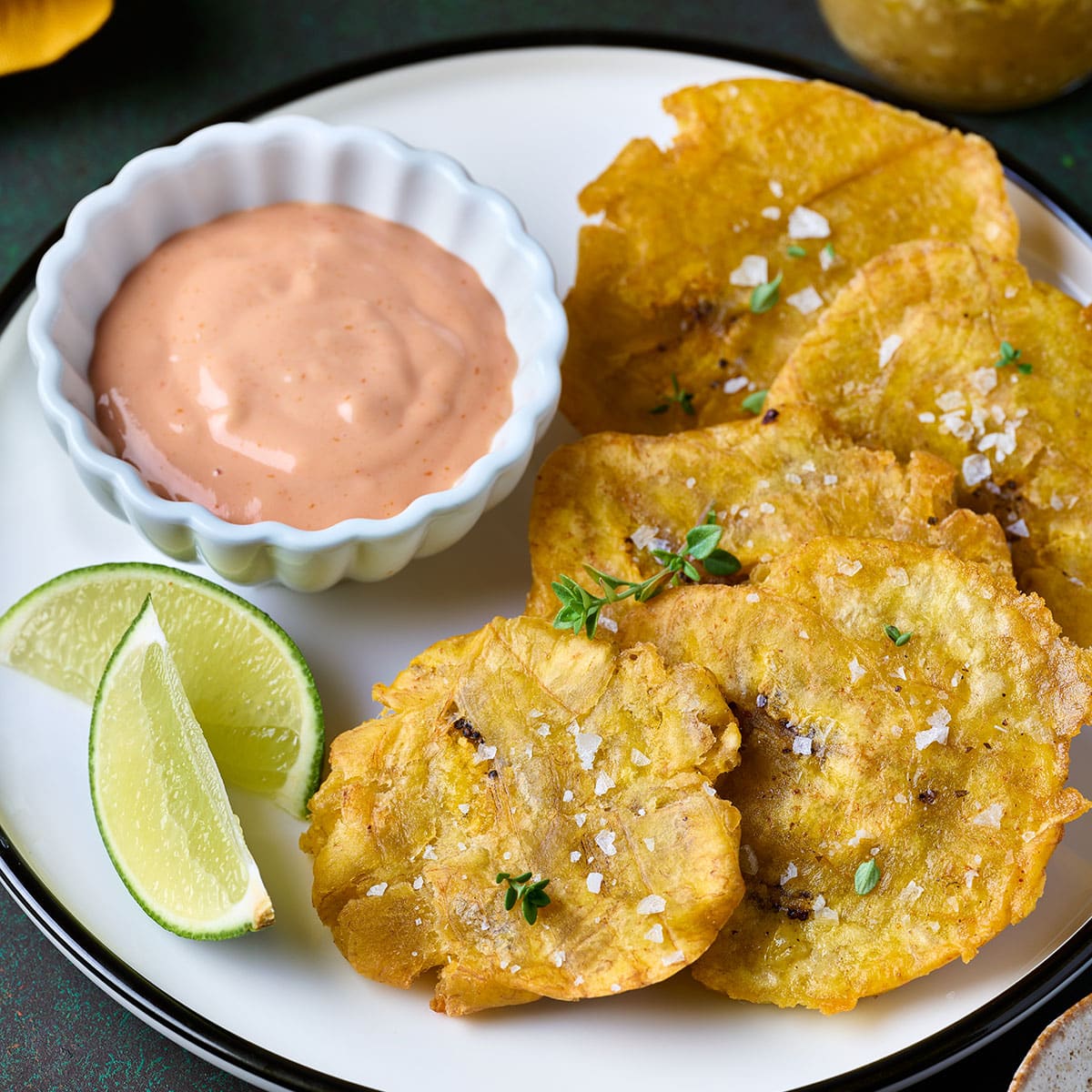 Fried green plantains on a plate with lemon slices and mayo ketchup on the side to dip the tostones in.