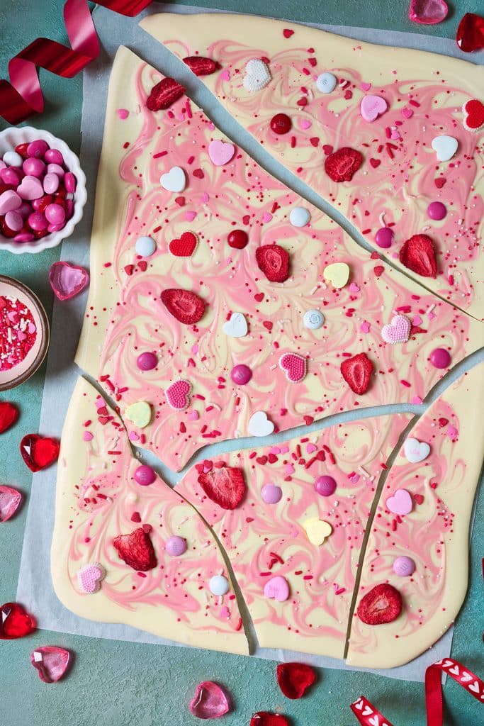 Valentine's day white chocolate bark with candies and freeze dried fruit on a sheet pan broken up into pieces.