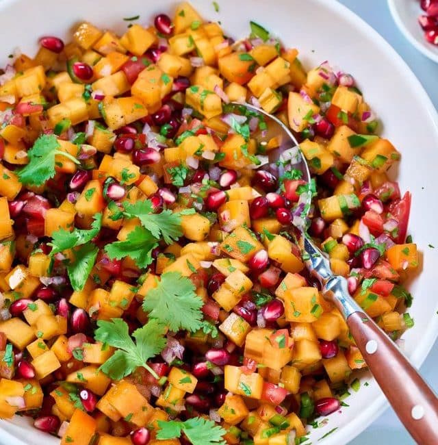A bowl filled with persimmon salsa fresca garnished with pomegranate arils and fresh cilantro.