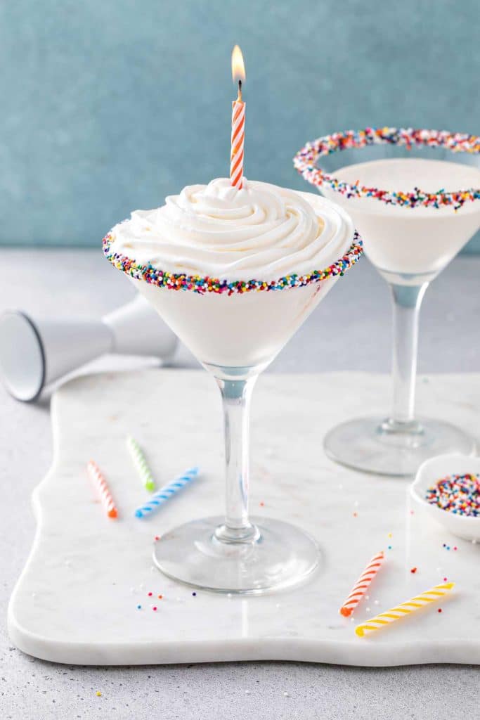 Birthday Cake Martini topped with a whipped cream and a lit birthday candle.