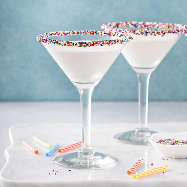 two martini glasses filled with birthday cake martini dipped in sprinkles