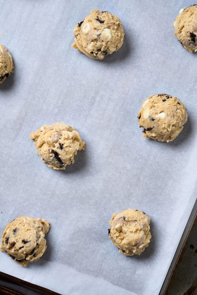 Unbaked cookie dough balls on a cookie sheet lined with parchment paper.