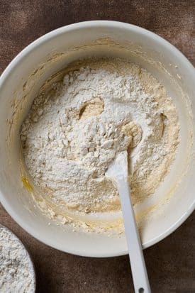 Adding dry ingredients into a mixing bowl with cookie dough