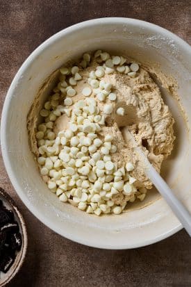Adding white chocolate chips to a bowl of cookie dough