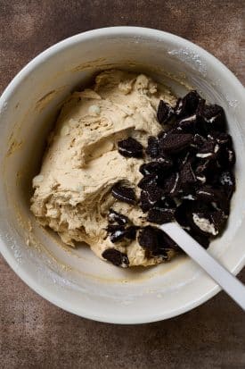 Oreo cookie chunks on top of cookie dough in a mixing bowl.
