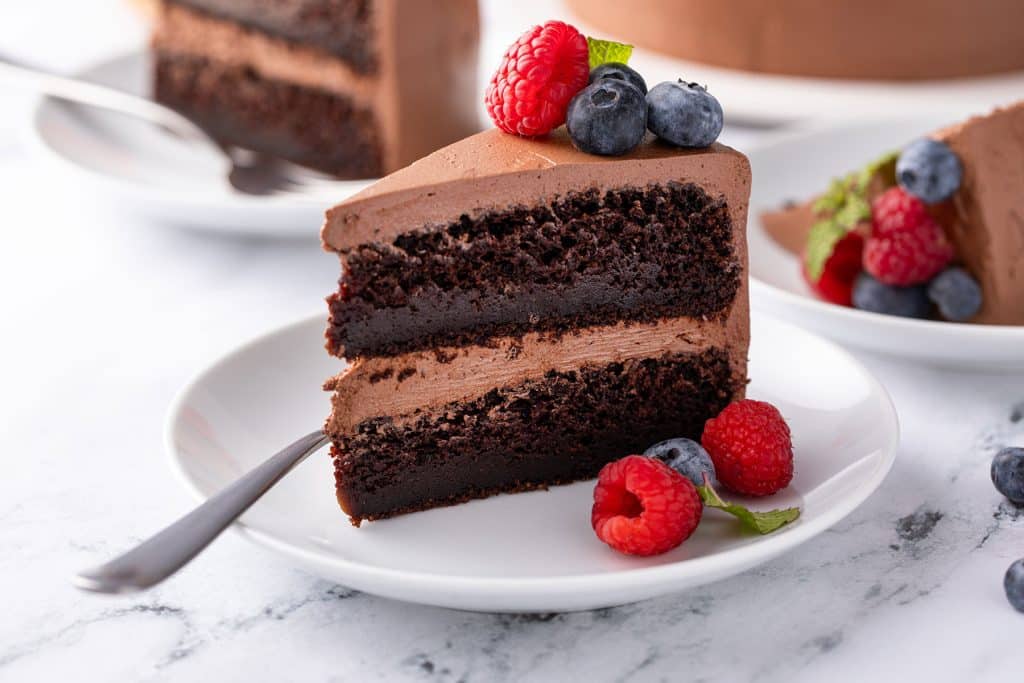 a slices of vegan chocolate cake with chocolate frosting decorated with berries