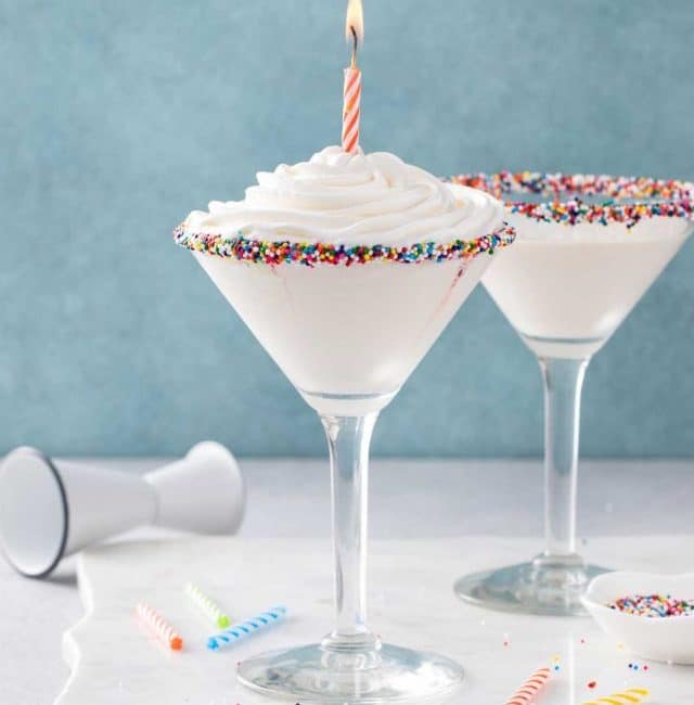 Birthday Cake Martini topped with a whipped cream and a lit birthday candle.