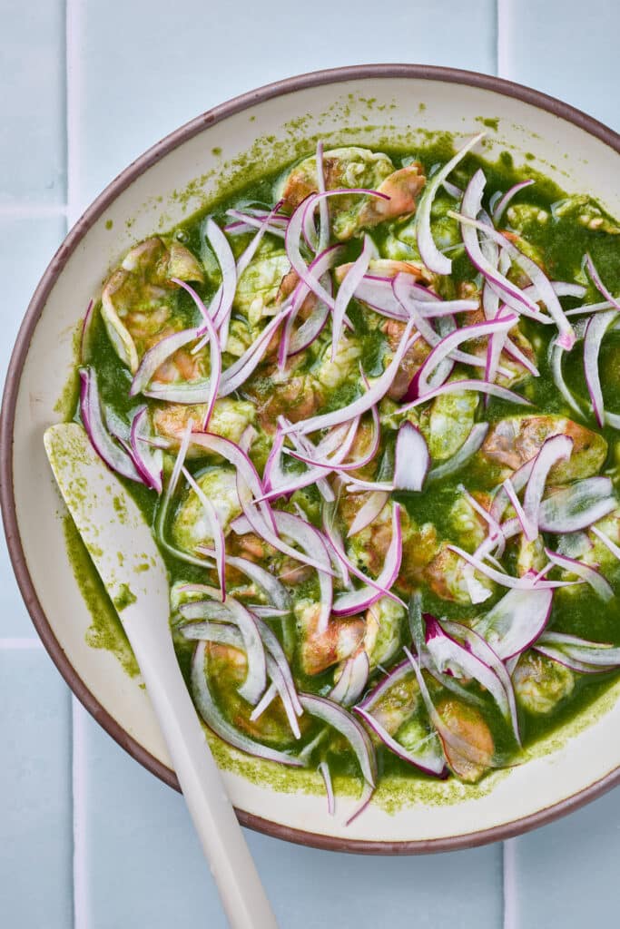 Shrimp coated in green aguachile sauce  and topped with sliced red onion.