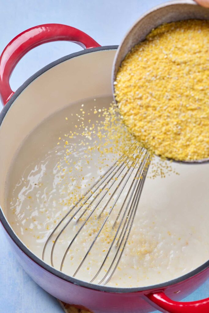 Adding yellow cornmeal into a pot filled with a broth and milk mixture