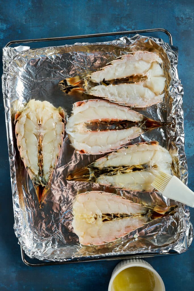 Brushing melted butter on lobster tails cut in half and set on a sheet pan