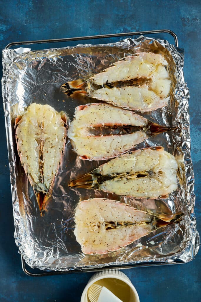 Lobster tails cut in half and seasoned with melted butter on a sheet pan