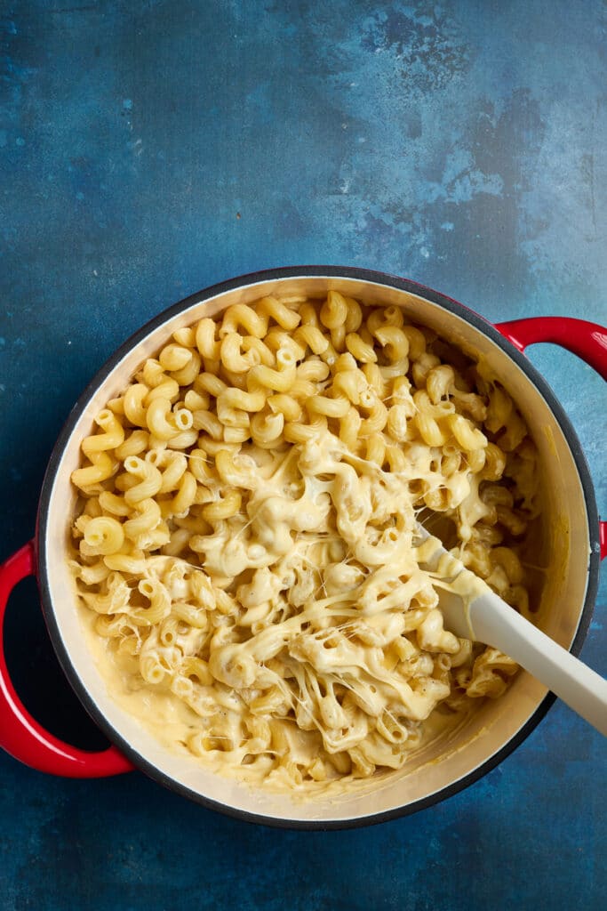 Combining pasta with cheese sauce in a pot.