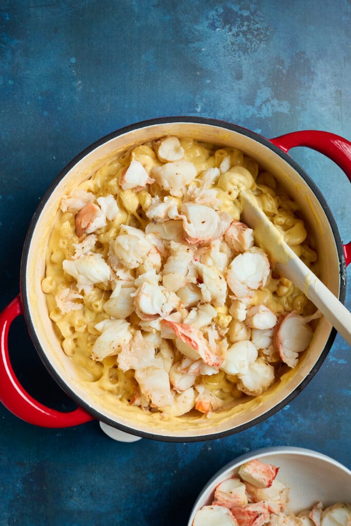Mixing bite size pieces of lobster meat into creamy macaroni an cheese in a pot