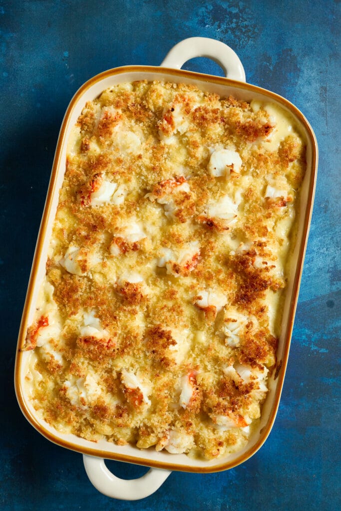 Lobster mac and cheese topped with golden brown buttery bread crumbs on a baking dish.
