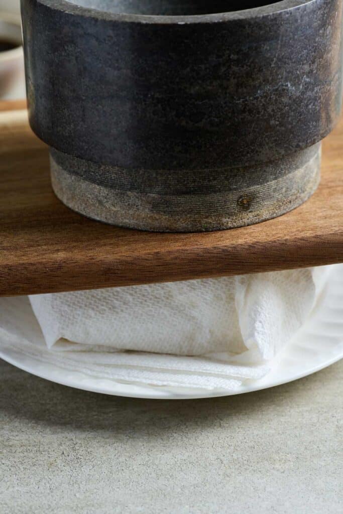 Pressing tofu weighted with a cutting board and a heavy pot.
