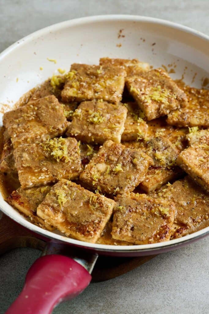 Crispy tofu topped with lemon zest in a skillet.