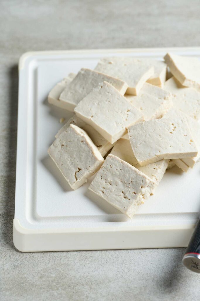 Thin pieces of tofu cut into squres on a cutting board.