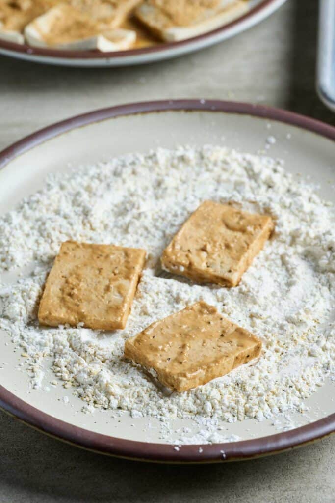Marinated Tofu on a plate of a cornstarch coating.