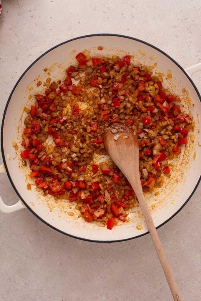 Blooming spices in a skillet with sautéed onions and red bell peppers