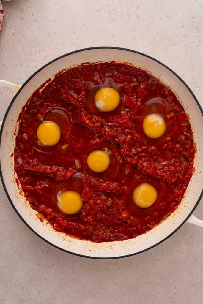 A skillet with a reduced tomato sauce topped with raw eggs