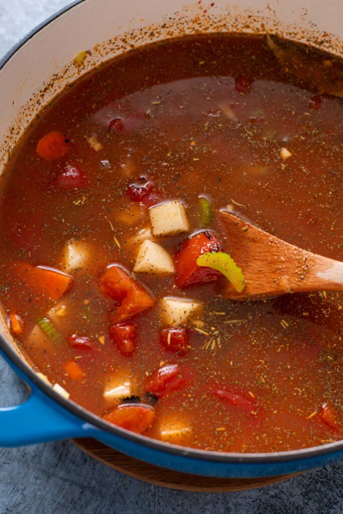 A Dutch oven with veggies and potatoes in a tomato based broth.