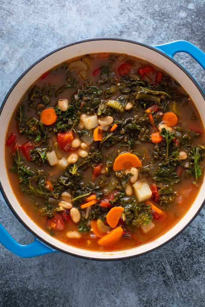 A Dutch oven with vegetables and bean soup with cooked kale in a creamy tomato based broth.