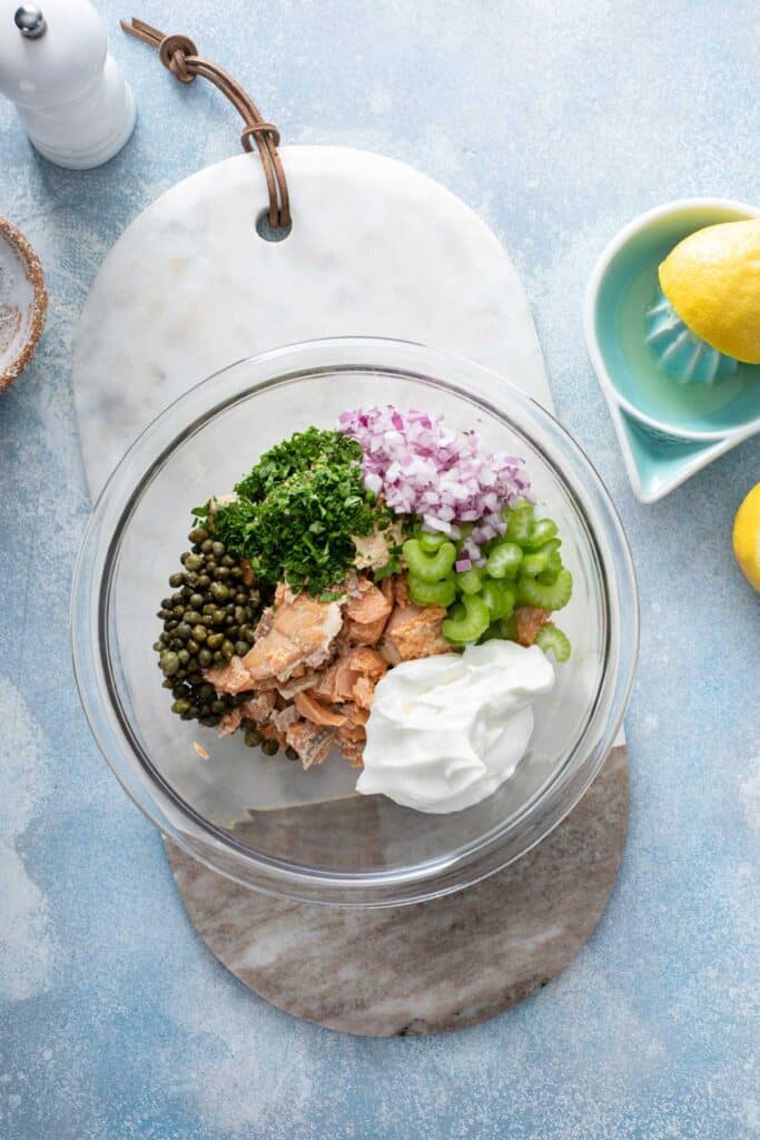 Flaky salmon, celery, chopped red onion, creamy yogurt, capers and fresh herbs in a glass bowl.