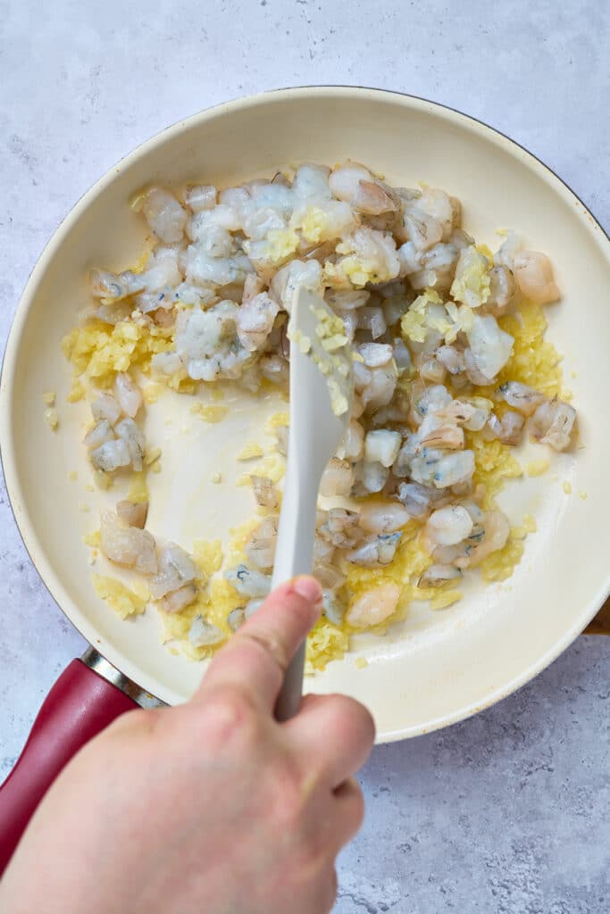 Chopped shrimp added into a skillet with sautéed onions and garlic.